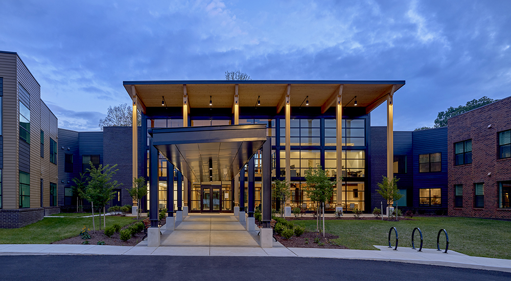 The Lodge at Autumn Willow entrance at dusk, with a glowing timber canopy and glass facade.