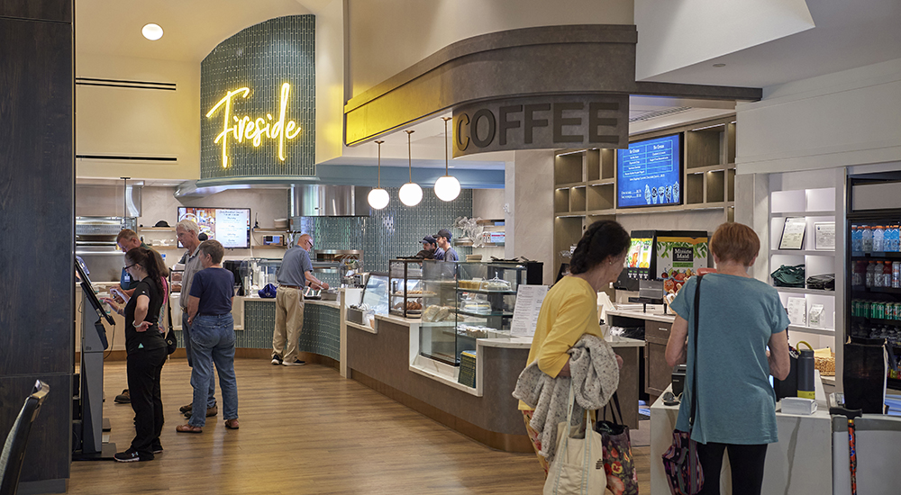 A cozy café at Medford Leas continuing care retirement community, with a neon sign reading 'Fireside' and customers ordering coffee and food.