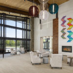 Community room at Tsali Care Center in Cherokee, North Carolina, featuring vaulted wood ceilings, a fireplace, colorful art, lounge seating, and large windows with mountain views.