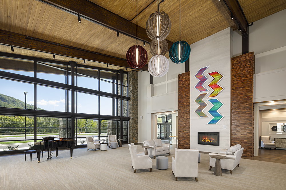 Community room at Tsali Care Center in Cherokee, North Carolina, featuring vaulted wood ceilings, a fireplace, colorful art, lounge seating, and large windows with mountain views.